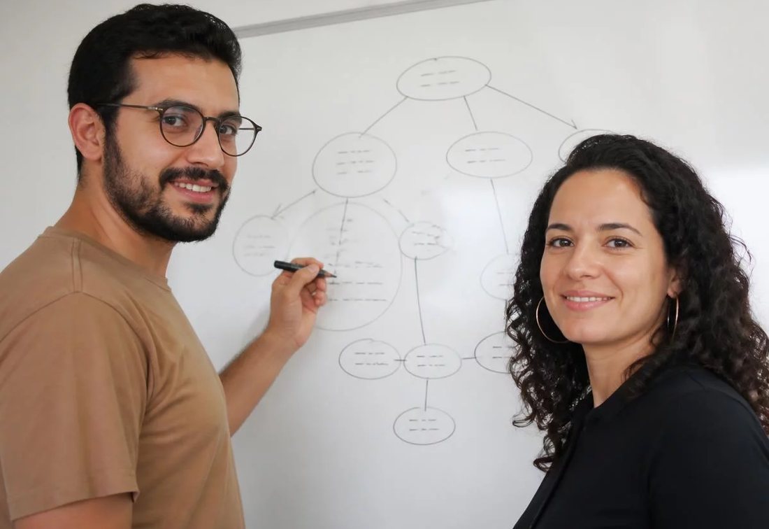 Dupla desenhando no quadro branco a estrutura de uma tese